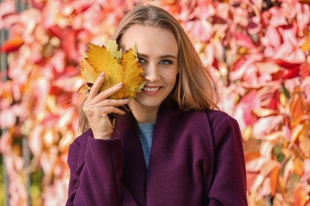 Beautiful young woman with autumn leaves in parkの写真素材