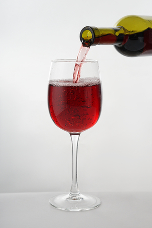 Pouring of tasty wine from bottle into glass on white backgroundの写真素材