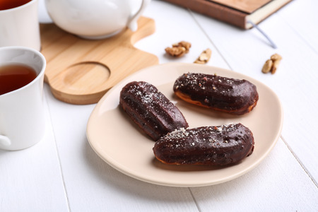 Plate with delicious eclairs and cup of tea on white wooden table