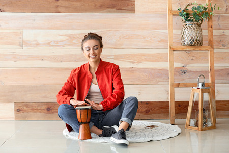 Beautiful woman playing tam-tam near wooden wall