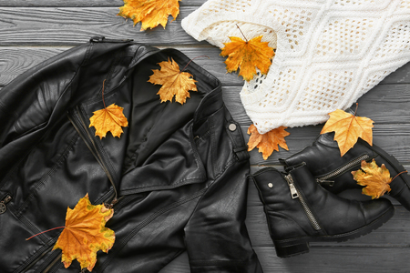 Stylish outfit with boots and autumn leaves on wooden background, top viewの写真素材