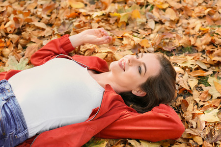 Beautiful young woman lying on fallen leaves in autumn parkの写真素材