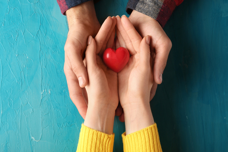 Loving young couple holding red heart on color backgroundの写真素材