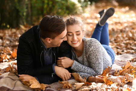 Loving young couple lying on plaid in autumn parkの写真素材