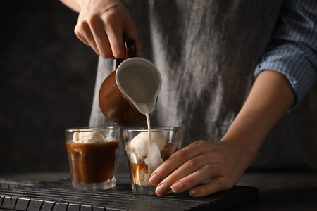 Woman pouring milk into glass with coffee and ice creamの写真素材