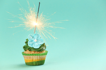 Tasty birthday cupcake with sparkler on color backgroundの写真素材