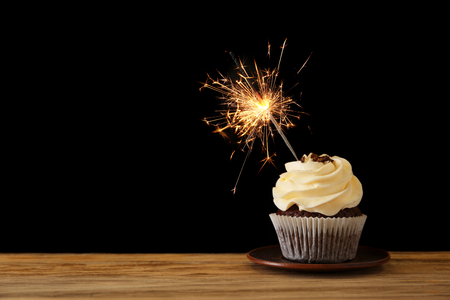 Tasty chocolate cupcake with sparkler on wooden table against dark backgroundの写真素材