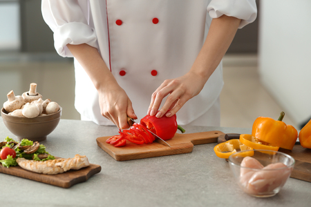 Young female chef cutting pepper in kitchenの写真素材