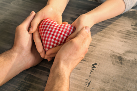 Loving young couple holding fabric heart on grey backgroundの写真素材