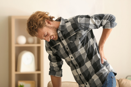 Young man suffering from back pain at homeの写真素材