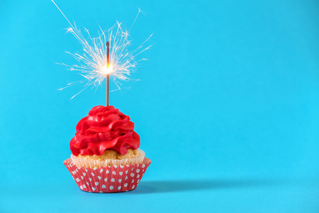 Tasty cupcake with sparkler on color backgroundの写真素材
