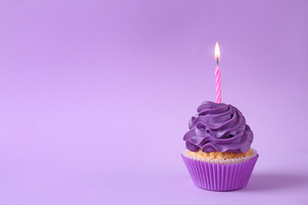 Tasty cupcake with burning candle on color backgroundの写真素材