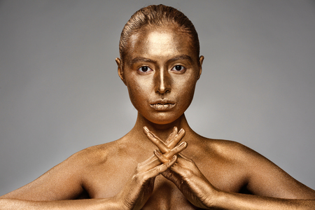 Beautiful young woman with golden paint on her body against grey backgroundの写真素材