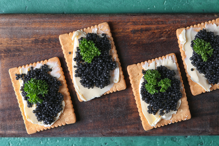 Delicious cookies with black caviar on wooden boardの写真素材