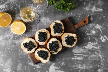 Delicious sandwiches with black caviar and glass of wine on grey tableの写真素材