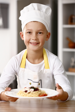 Cute little chef with tasty dish in kitchenの写真素材