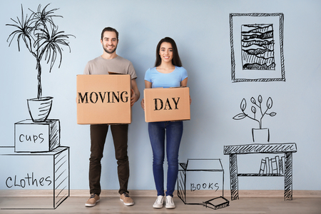 Young couple holding boxes with text MOVING DAY indoors and imagining interior of new houseの写真素材