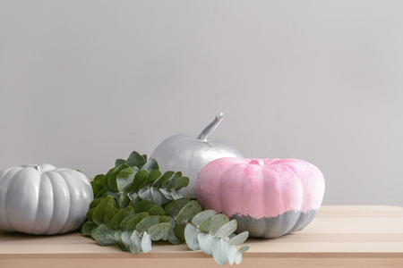 Painted pumpkins with green branches on wooden table against grey wallの写真素材