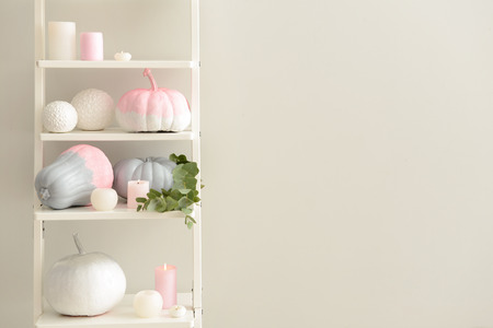 Painted pumpkins with burning candles on shelving near light wallの写真素材