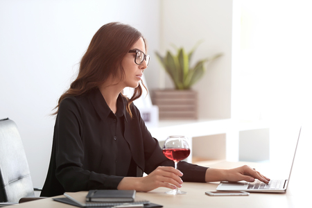 Beautiful young woman drinking wine in officeの写真素材