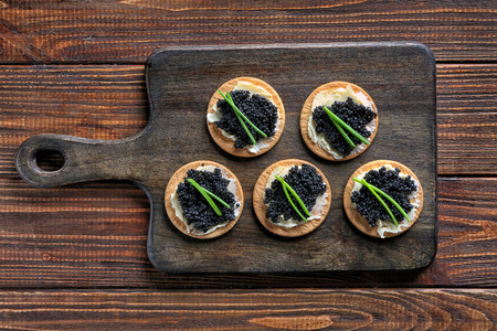 Delicious cookies with black caviar on wooden boardの写真素材
