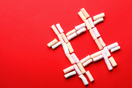Hashtag sign made of marshmallows on color background