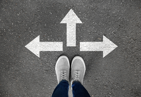 Woman standing on asphalt road with arrows pointing in different directions. Concept of choice