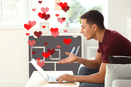 Young man using laptop for online dating at homeの写真素材