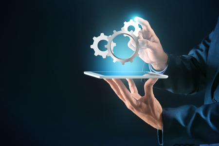 Businessman with tablet PC and digital gearwheels on dark background. Concept of Internet and technical support serviceの写真素材