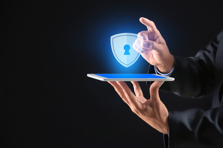 Businessman with tablet PC and shield icon on dark background. Data security concept
