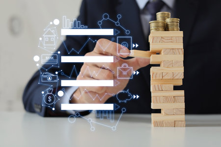 Male bank manager with tower made of blocks and coins at table in office. Concept of planning, risk...