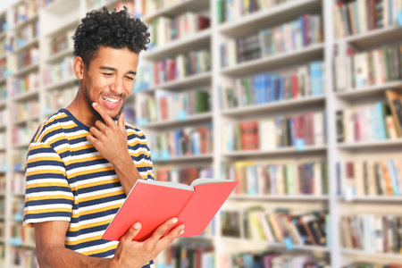 Portrait of happy African-American man with book in modern library