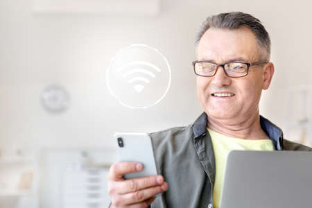 Mature man with laptop and mobile phone using wifi at homeの写真素材