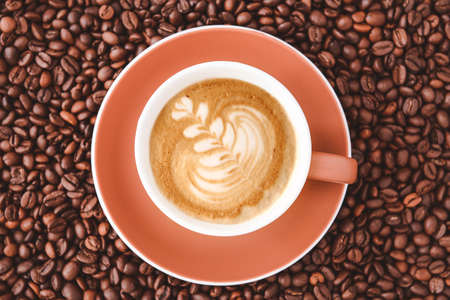 Cup of tasty cappuccino on coffee beans, top viewの写真素材