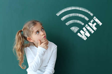 Thoughtful little schoolgirl near blackboard with drawn wifi symbol in classroom