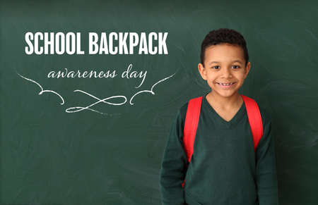 Cute African-American boy near blackboard with text SCHOOL BACKPACK AWARENESS DAY