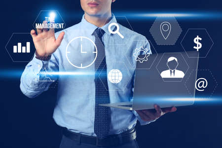 Businessman with laptop using virtual screen on dark background. Time management conceptの写真素材