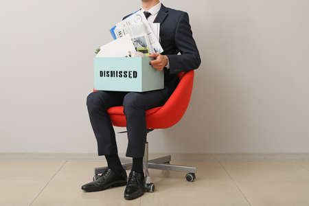 Fired worker with personal things sitting on chair near light wallの写真素材