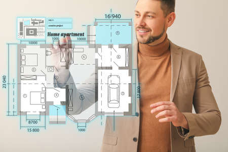 Male architect with virtual plan of building on light background