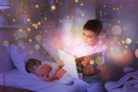 Little girl falling asleep while her brother reading bedtime story at homeの写真素材