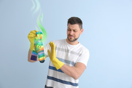 Displeased man with dirty stinky socks on light background