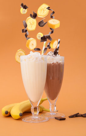 Glasses of tasty milkshakes and falling ingredients on color backgroundの写真素材