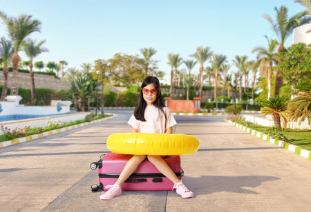 Cute girl with suitcase and inflatable ring at tropical resortの写真素材