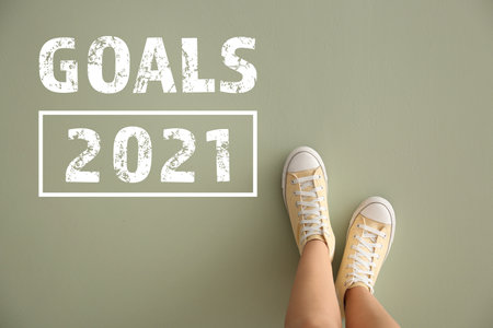 Legs of woman in casual shoes and text GOALS 2021 on color background