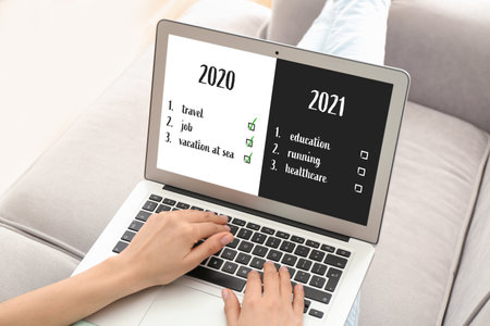 Young woman with laptop making to do list on 2021 year at home