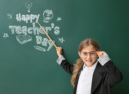 Cute little schoolgirl with pointer near blackboard with text HAPPY TEACHER'S DAY in classroomの写真素材