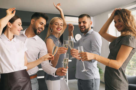 Young people clinking glasses of tasty champagne at party in officeの写真素材