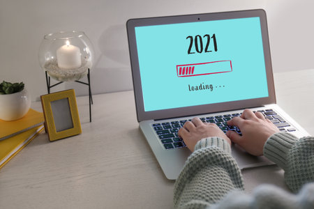 Young woman with laptop making to do list on 2021 year at home