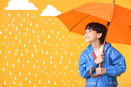 Cute little boy in raincoat and with umbrella on color background with drawn rain dropsの写真素材