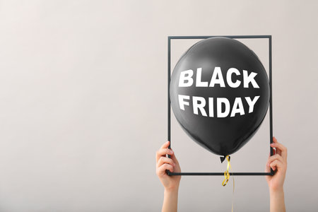 Hands holding frame and balloon with text BLACK FRIDAY on gray backgroundの写真素材